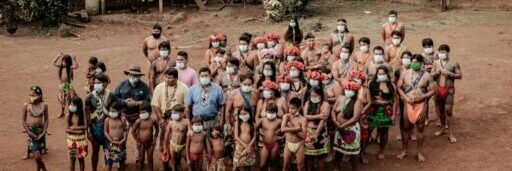 Aerial view of indigenous people in traditional attire gathered in a rural village setting.